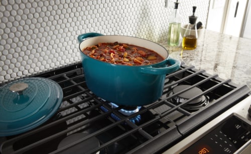 Blue dutch oven full of stew on iron grates above gas burner 
