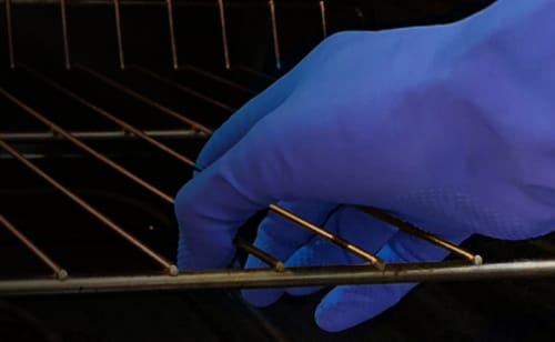 Hand wearing blue glove removing oven rack from oven cavity