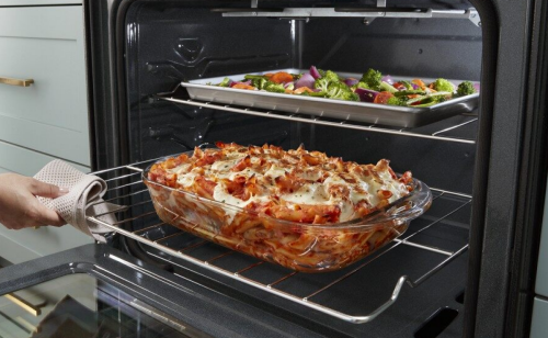 A tray of roasted vegetables and tray of baked lasagna on oven racks.
