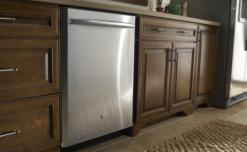 A stainless steel dishwasher with a bar handle surrounded by wood cabinetry