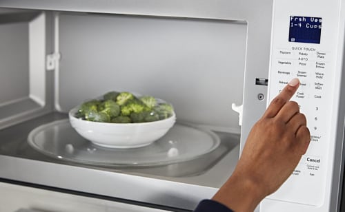 A person programming a Maytag® microwave with a bowl of broccoli