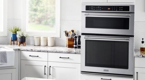A Maytag® wall oven microwave combo placed between white cabinets with gray countertops