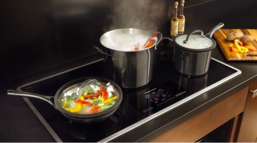 Pots and pans full of food cooking on a KitchenAid® induction cooktop.