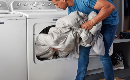 A person loading a comforter into a Maytag® front load dryer