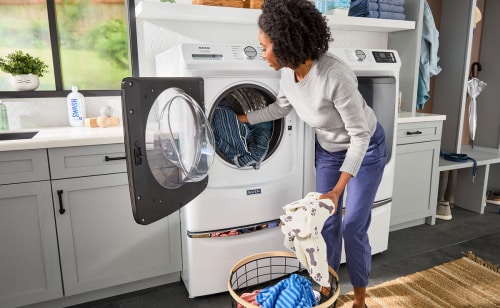 Person loading clothes into a white Maytag® front load washer