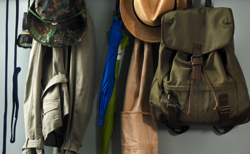 A closeup of a coat rack with jackets, a canvas backpack and hat.