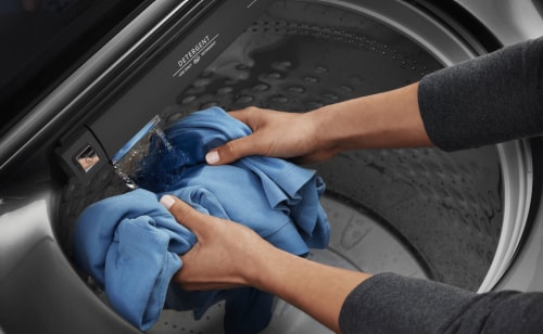 Person rinsing garment with built-in faucet on Maytag® top load washer