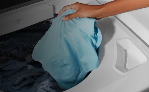 A person placing a laundry item into a washing machine