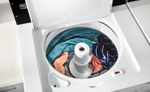 A load of orange, turquoise and blue clothes in a top load washer with an agitator