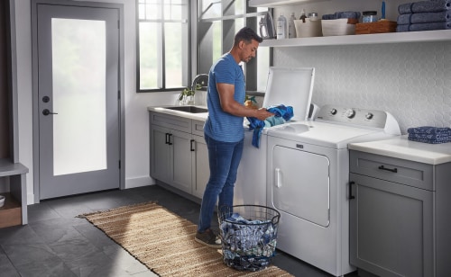 A man loading clothes into his white, top-load washer