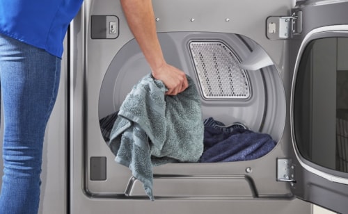 A person placing a blue towel into a dryer