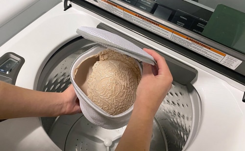 Person holding mesh laundry bag over open washer