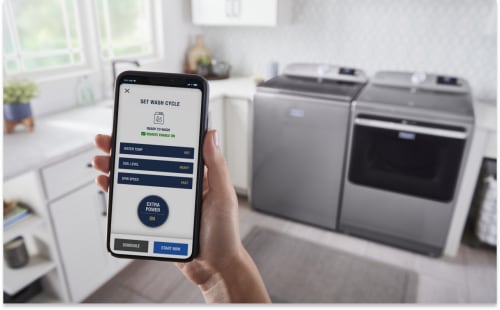 Person using the Maytag™ App standing in front of a gray top-load laundry pair