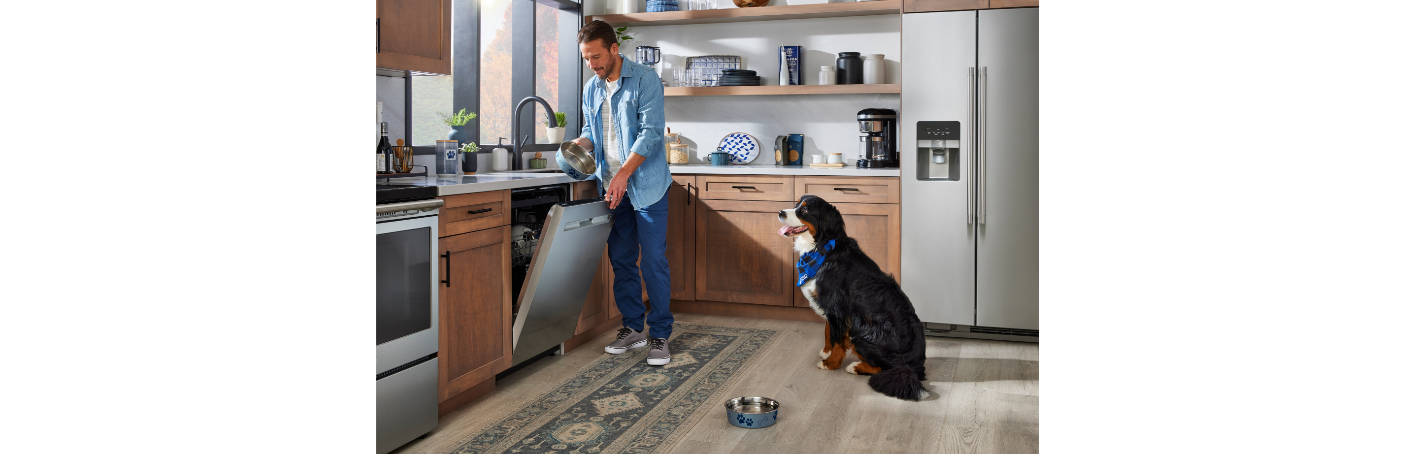 A person loading their Maytag® dishwasher with a dog in the kitchen