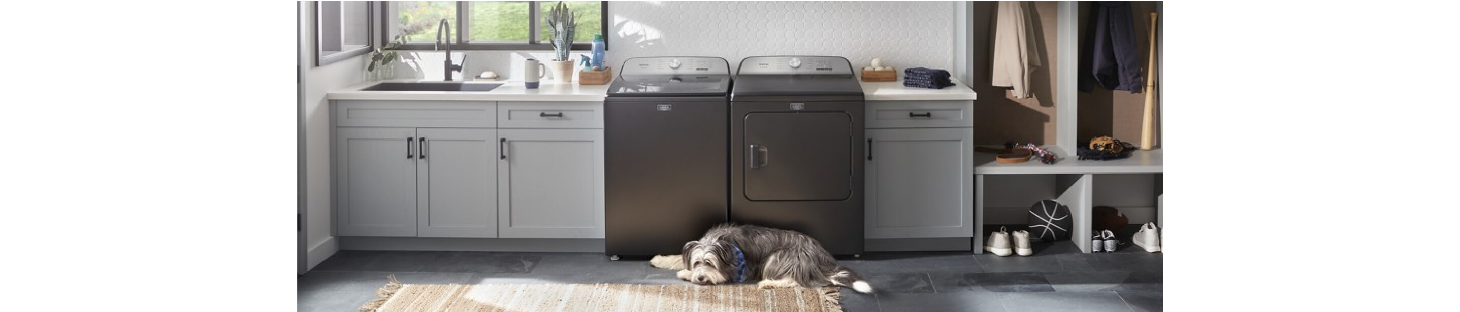 A Maytag® washer and dryer in a laundry room with white cabinets and dog laying on the floor 