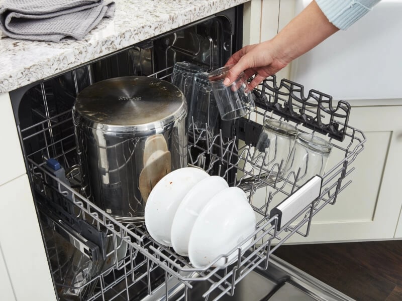 Person loading glass into top rack of dishwasher