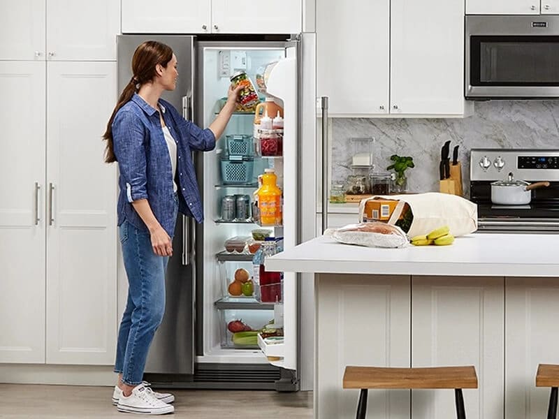 Person placing a jar in a side-by-side refrigerator