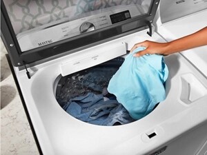 Woman’s hand dropping clothing into Maytag® washing machine