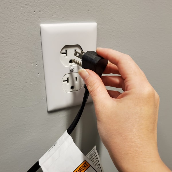 A hand unplugging a refrigerator cord from an outlet.