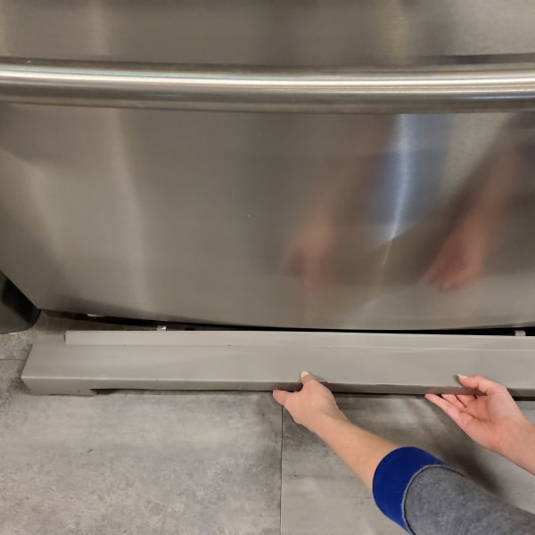 Hands removing the base grille on a refrigerator.