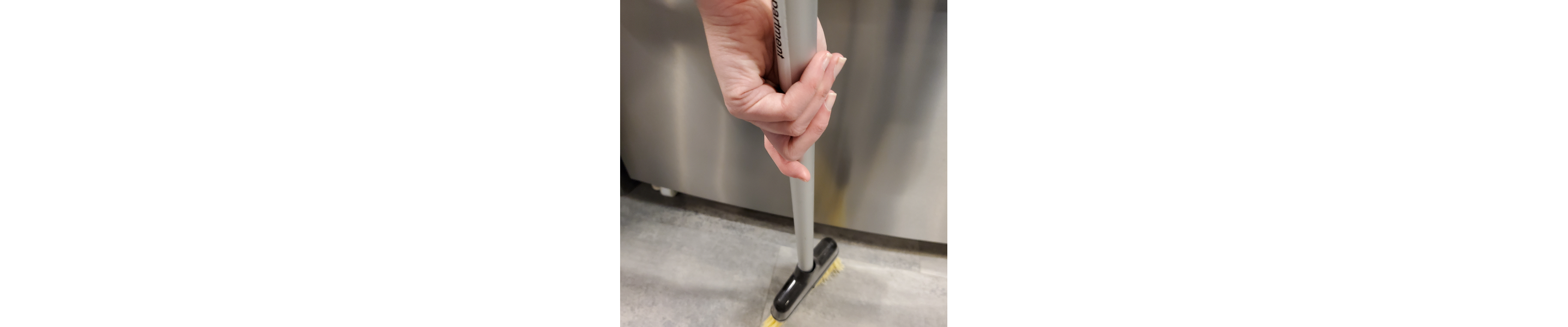 A broom sweeping the floor behind a refrigerator.