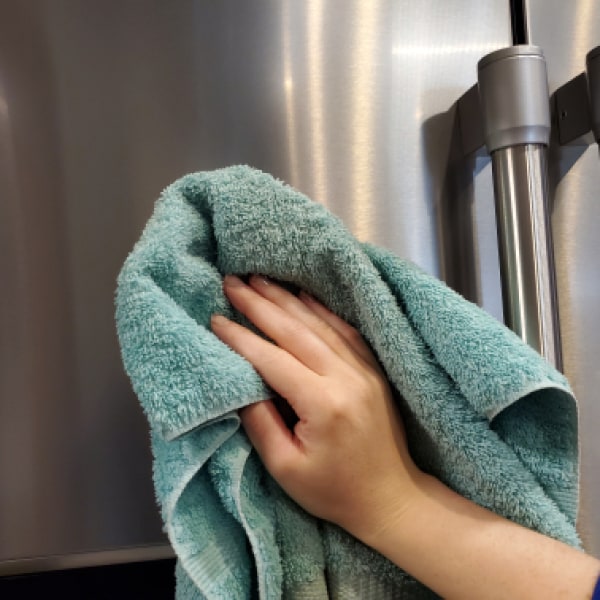 A hand drying the outside of a refrigerator door with a cloth.