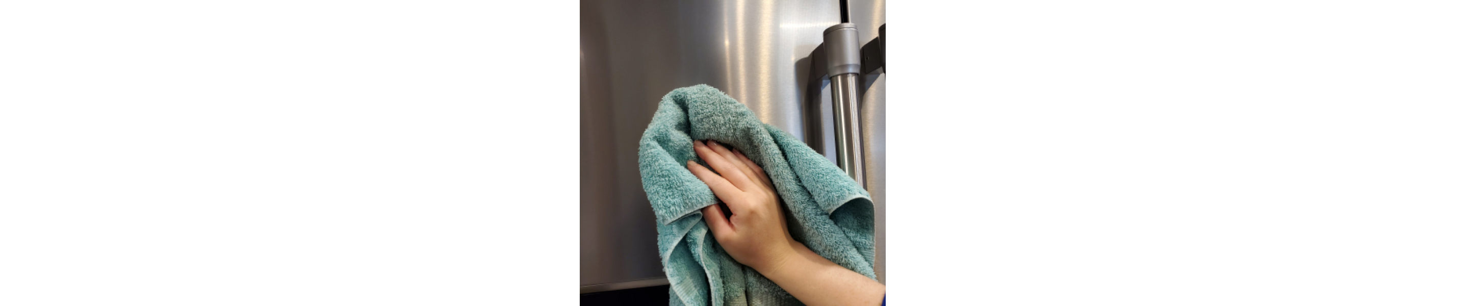 A hand drying the outside of a refrigerator door with a cloth.