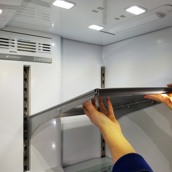 Hands lifting a shelf out of a fridge.