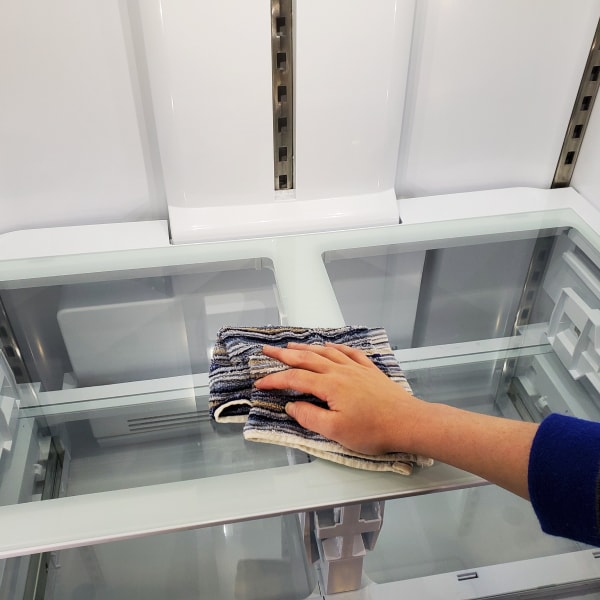 A hand wiping a refrigerator shelf.