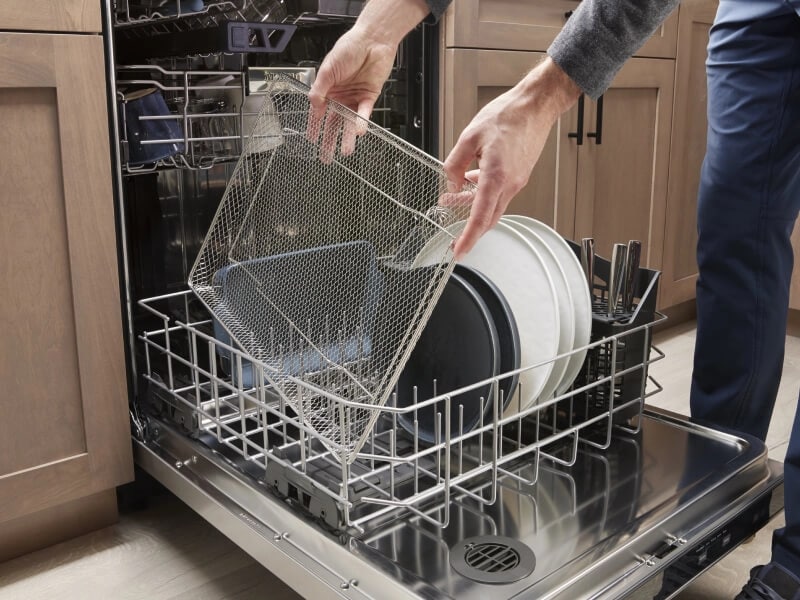 Person loading dishes into bottom rack of open dishwasher