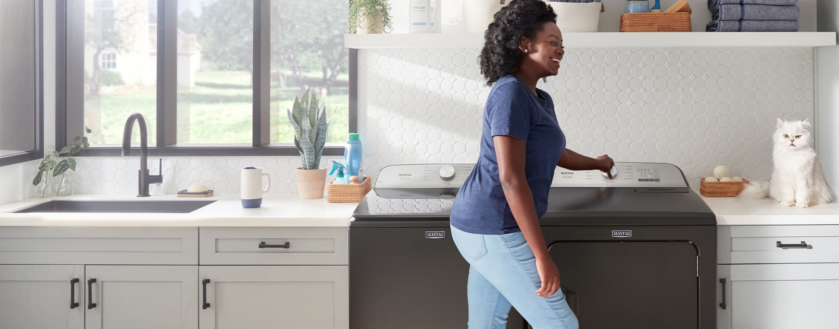 A woman doing laundry with a Maytag® washer and dryer set.