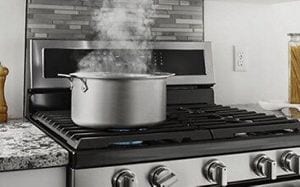 Pot with steam coming off it on top of a gas range.