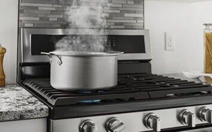 Pot with steam coming off it on top of a gas range.