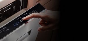 A person selecting an option on a dishwasher.