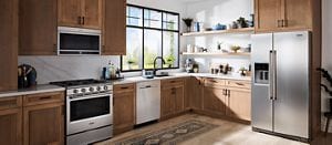 A stainless steel Maytag® kitchen suite installed in a kitchen with light wood cabinets.