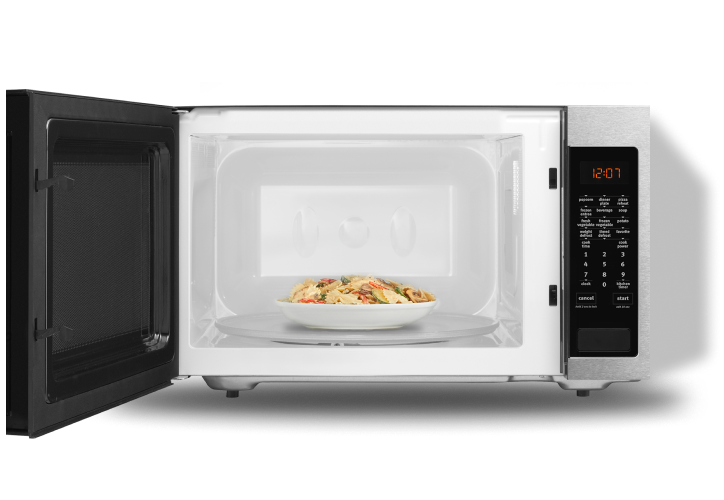 An open microwave with a plate of pasta inside.