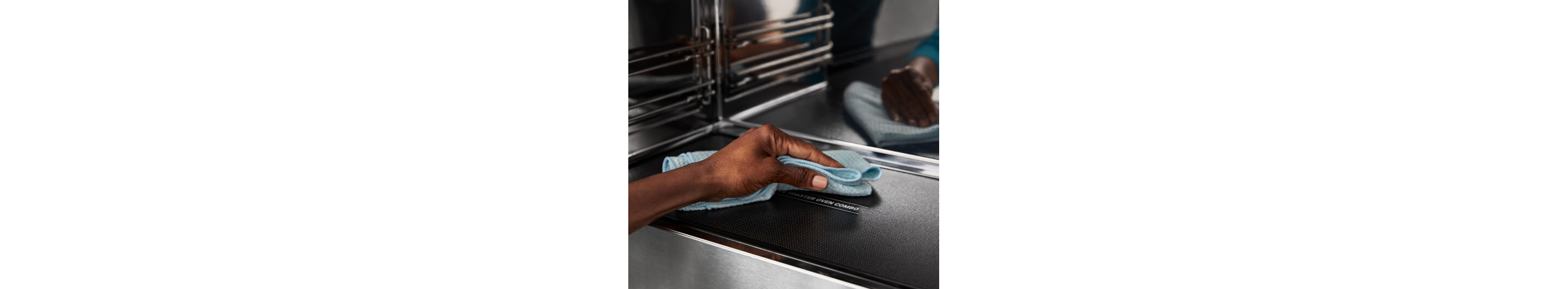 A hand holding a towel, cleaning the bottom of a microwave oven.