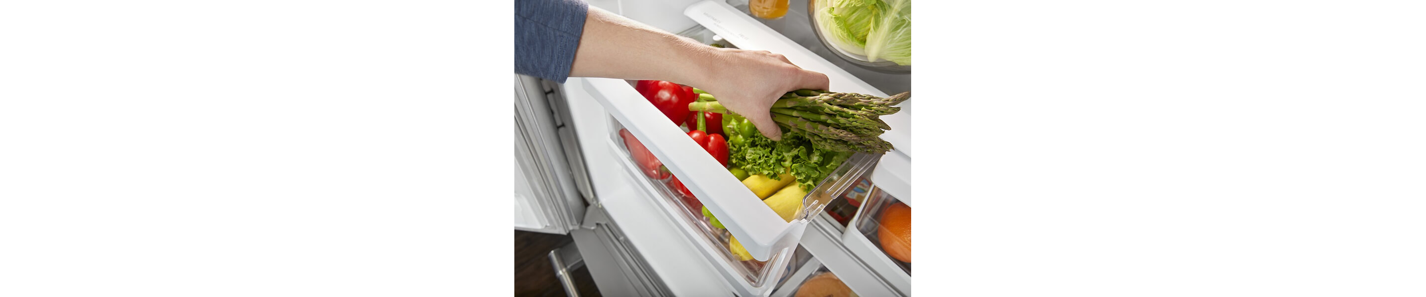 Person placing a bundle of asparagus inside a refrigerator drawer