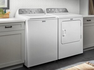 A white Maytag® top load washer and dryer next to grey cabinetry