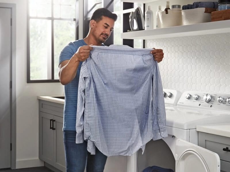 A person holding up a shirt in front of their dryer