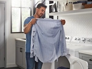A person holding up a shirt in front of their dryer
