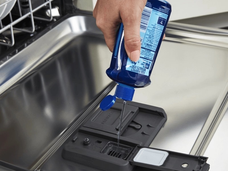 Person adding dishwasher detergent to a detergent dispenser