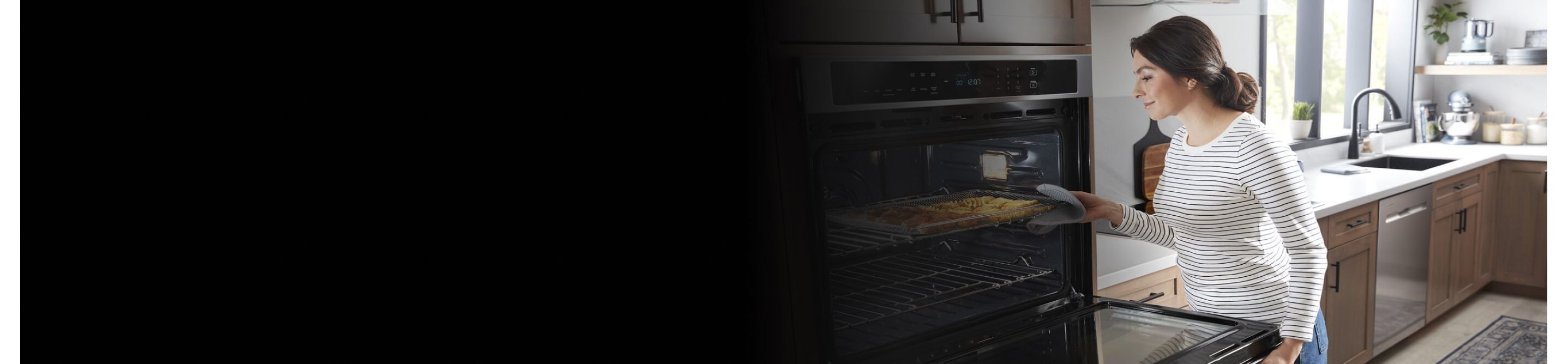 Person removing a baking tray from a Maytag® wall oven