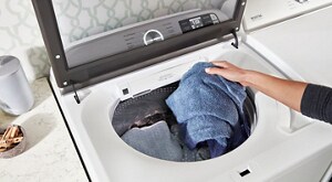 Person putting clothes in a top load washer