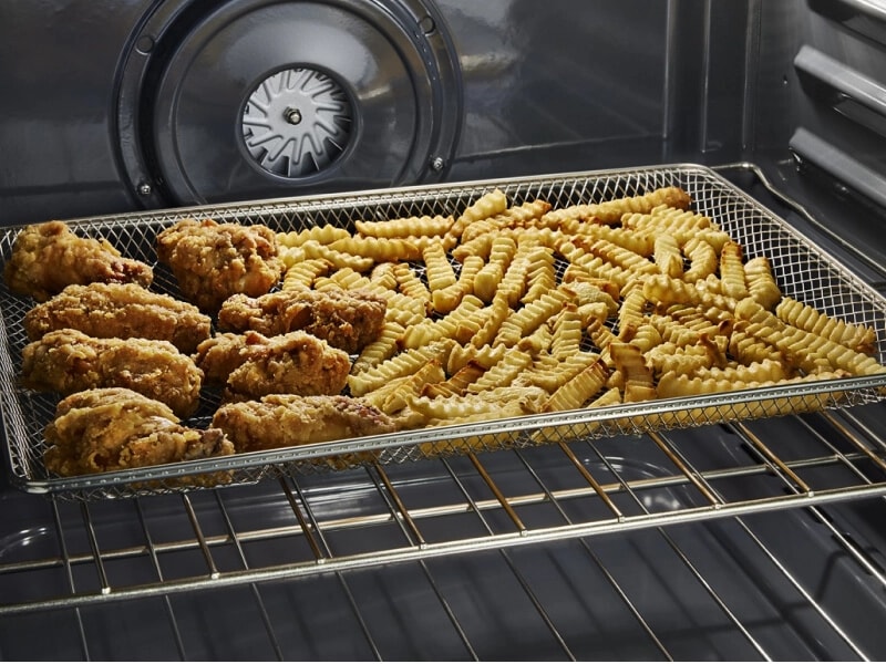 Close-up of chicken and french fries in an air fry basket inside the oven