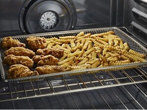 Close-up of chicken and french fries in an air fry basket inside the oven