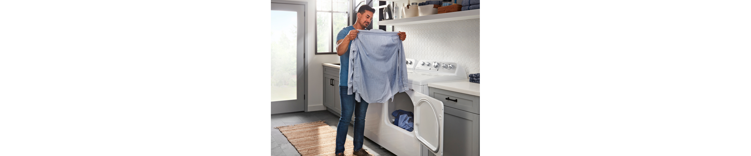 Person removes blue shirt from a Maytag® dryer in laundry room