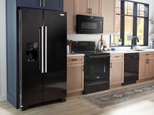Suite of black Maytag® appliances in a kitchen with brown cabinetry
