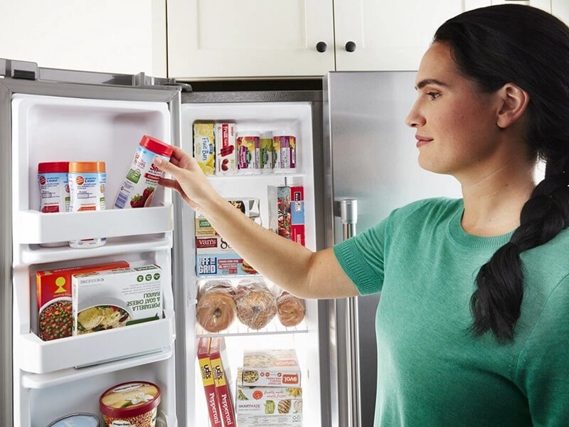 Close-up of person placing an item in the freezer door bin on a side-by-side refrigerator