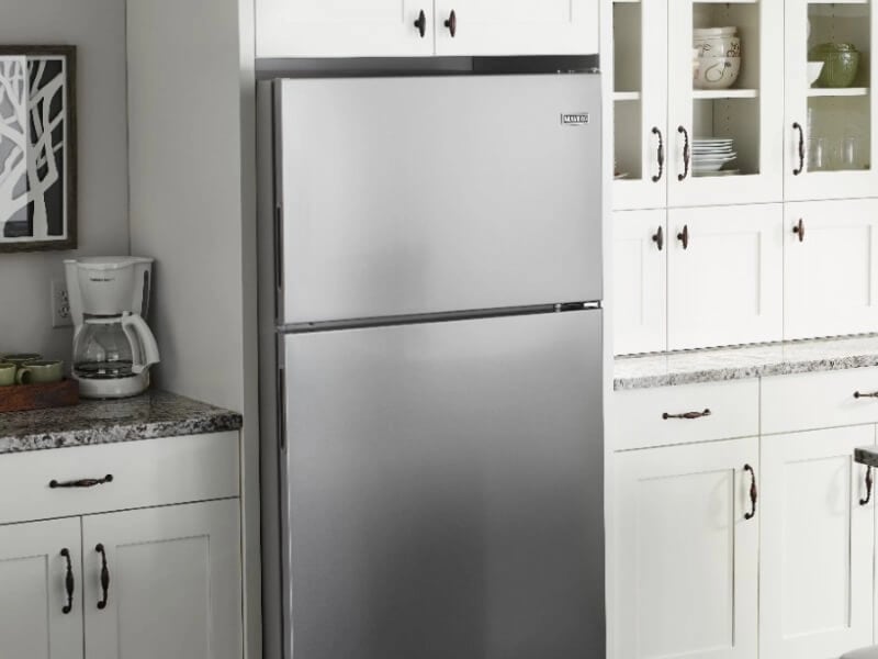 Stainless steel Maytag brand top-freezer refrigerator in kitchen with white cabinets